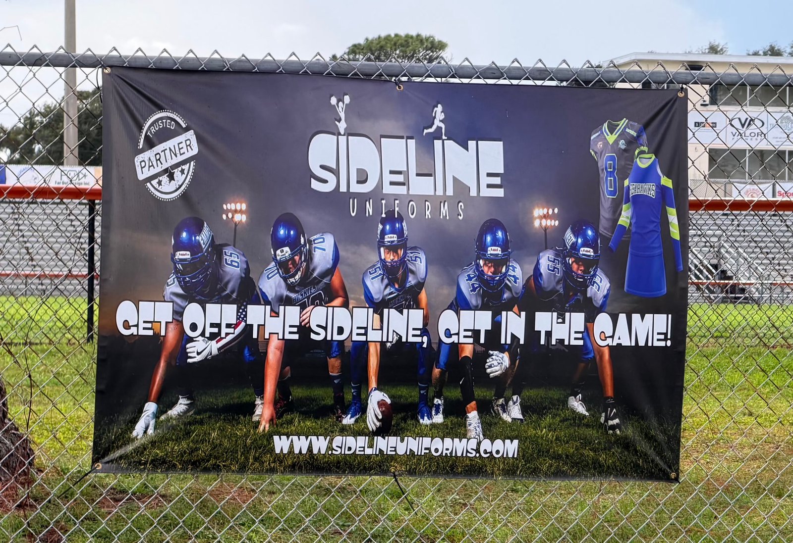 Sideline Uniforms banner on a fence
